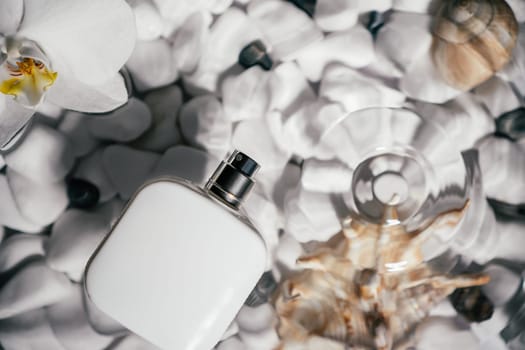 White square perfume bottle, vial in transparent fresh water with flecks and waves above bottom of white stones and shell. Skin care protection. Flat lay.