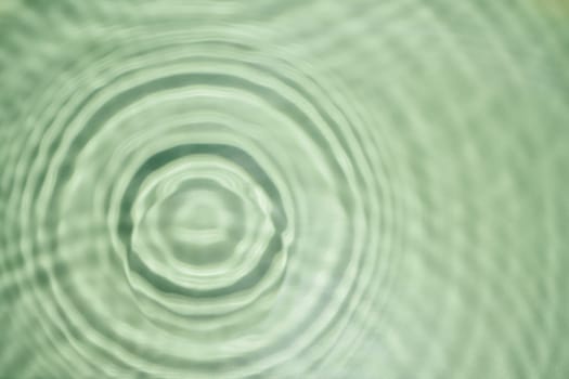 Defocused rippled transparent fresh green water gel surface in swimming pool with flecks, waves, shade. Concentric expanding circles on surface from fallen drop. Health care on sea coast. Copy space