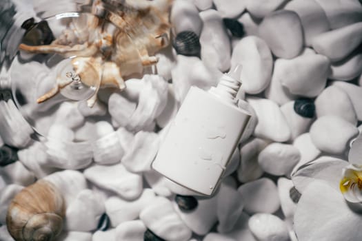 White beauty product sunscreen cream vial tube bottle on transparent fresh water with flecks and waves, bottom of white stones and shells. Face and body skin care, moisturizing cosmetic. Top view
