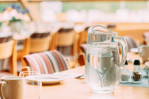 Cozy Interior Of Summer Cafe. Jug Of Icy Cold Ice Water On Table And Cutlery Laid Out.