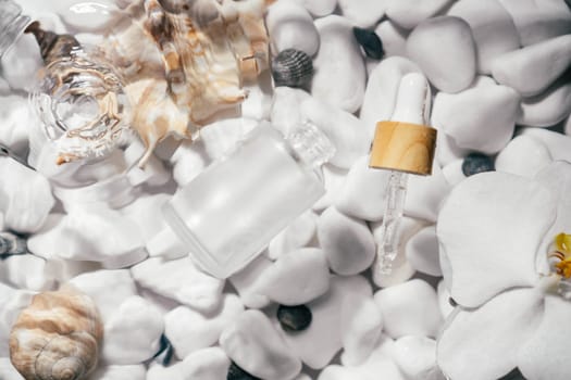 Facial pipette serum oil, essence cosmetic product in bottle on transparent fresh water with fleck and waves, bottom of white stones and shells. Organic skin body antiage care in hot climate. Top view