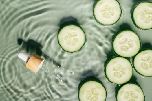 Facial pipette serum, whey beauty product near cucumber slices in water splashing fresh transparent, flecks. Flat lay, top view. Summer beach. Organic skin face and body moisturizing and rejuvenating