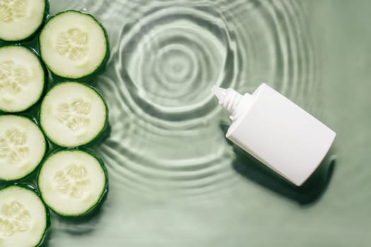White beauty product cream vial tube bottle with rows of cucumber slices on surface of rippled transparent fresh green water gel with fleck, wave, shadow. Concentric expanding circles from fallen drop