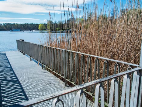 Perspective landscape view over a metal fence boat dock next to reed plants on the Flakensee near Woltersdorf in Brandenburg.