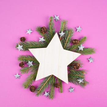 Christmas holiday background with a star, frame with fir branches and pine cones, winter season greeting card in pink