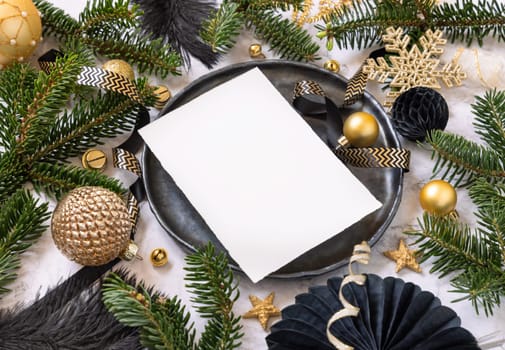 Black and golden Table setting with ornaments and fir tree branches, card mockup. Christmas or New Year invitation or meny on marble table close up, copy space. Winter holiday catering