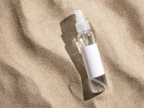 Spray bottle with blank label on beige sand top view, hard light. Package mockup. Natural skincare or SPA product. Facial cosmetics for beauty routine. Zen style with waves on sand, minimal aesthetic
