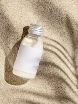 Cosmetic Cream bottle with blank label on beige sand top view. Packaging mockup. Natural skincare product for beauty routine. Summer sunny day with palm leaf hard shadow, tropical vacation mood