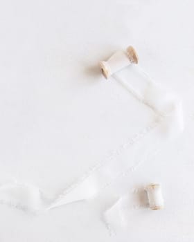 Silk ribbons with wooden bobbins on white top view, copy space. Romantic scene for wedding, valentines or mothers day cards