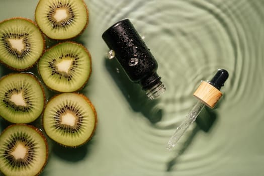 Facial pipette serum black bottle, whey beauty product near fruit tropical kiwi slices in water splashing fresh transparent, flecks. Top view. Organic skin face and body moisturizing and rejuvenating