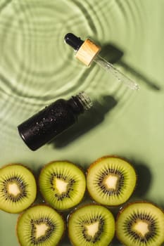Facial pipette serum black bottle, whey beauty product near fruit tropical kiwi slices in water splashing fresh transparent, flecks. Top view. Organic skin face and body moisturizing. Vertical