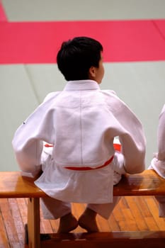 A karate kid sitting on bench and watching the competition