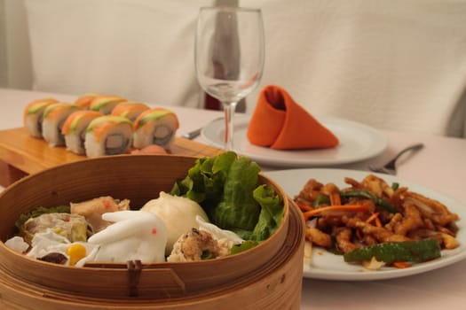 wontons in wooden bowl with sushi set and fried vegetables