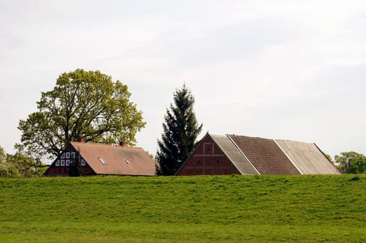 The roof of a barn and a house behind a green dike.