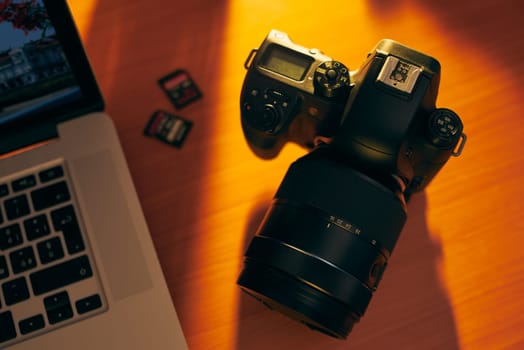 Still life of dslr camera, sdhc flash memories and laptop computer on wooden table. High angle view of objects with sunset lighting
