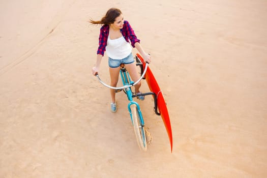 Surfer young woman riding her bicycle on the beach