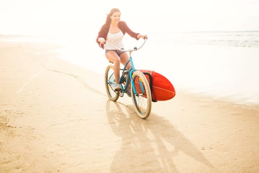 Surfer young woman riding her bicycle on the beach