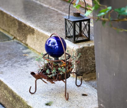 A garden decoration with a lantern and a glass ball in front of a stone staircase.