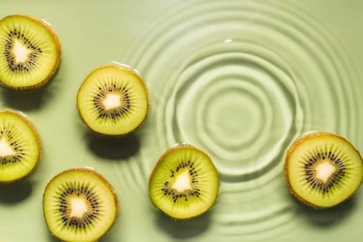 Kiwi slices lie on surface of rippled transparent fresh green exhilarant water gel with flecks, waves, shadow. Concentric expanding circles on surface from fallen drop. Health care. Copy space