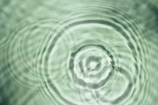 Defocused rippled transparent fresh green water gel surface in swimming pool with flecks, waves, shade. Concentric expanding circles on surface from fallen drop. Health care on sea coast. Copy space