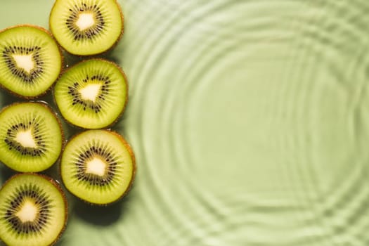 Kiwi slices lie on surface of rippled transparent fresh green exhilarant water gel with flecks, waves, shadow. Concentric expanding circles on surface from fallen drop. Health care. Copy space