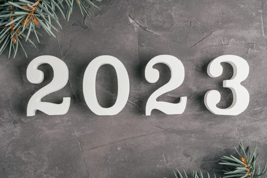 Happy New Year 2023. White wooden numbers 2023 lying on gray uneven concrete surface with Christmas tree branches. Merry Christmas. Top view