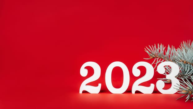 Happy New Year 2023. Bright red rectangular banner with white wooden numbers 2023 stand with Christmas tree branches. Merry Christmas. Copy space. Place for text