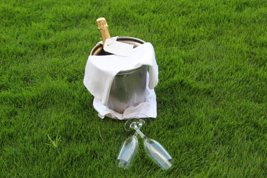 There is a champagne bottle in a champagne cooler and two glasses in front of it.