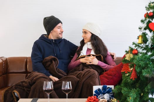 Romantic couple sitting on sofa and celebrating with glasses of red wine in living room. Winter holiday and Christmas eve together concept