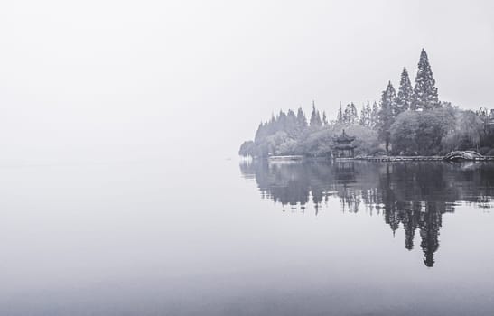 Panorama scenery of Morning fall nature misty foggy scene: forest with trees surrounded by  mist on the water surface of lake with hills and