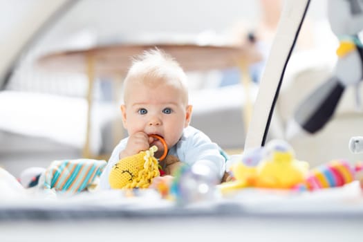 Cute baby boy playing with hanging toys arch on mat at home Baby activity and play center for early infant development. Baby playing at home.