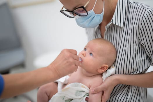 Pediatrician administring oral vaccination against rotavirus infection to little baby in presence of his mother. Children health care and disease prevention.