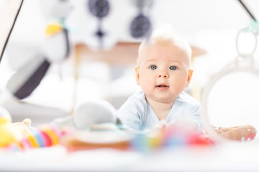 Cute baby boy playing with hanging toys arch on mat at home Baby activity and play center for early infant development. Baby playing at home.