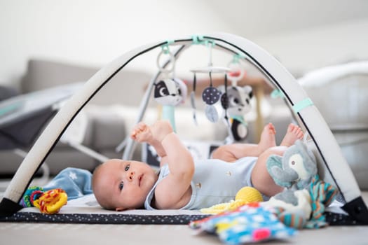 Cute baby boy playing with hanging toys arch on mat at home Baby activity and play center for early infant development. Baby playing at home.