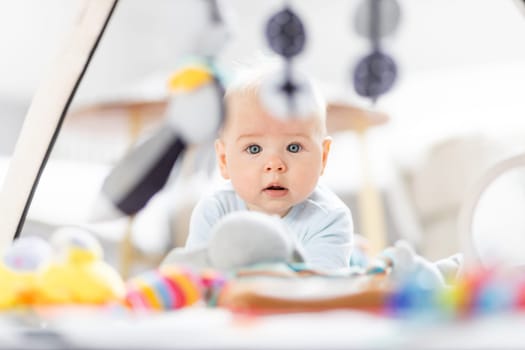 Cute baby boy playing with hanging toys arch on mat at home Baby activity and play center for early infant development. Baby playing at home.