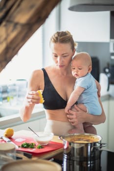 Woman cooking while holding four months old baby boy in her hands.