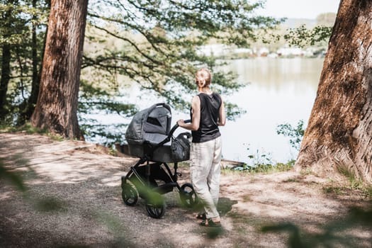 Rear view of casualy dressed mother walking with baby stroller in city park. Family, child and parenthood concept