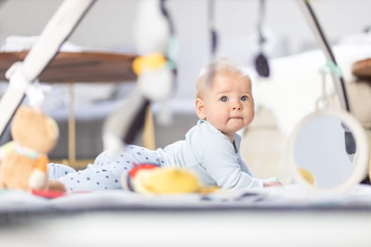 Cute baby boy playing with hanging toys arch on mat at home Baby activity and play center for early infant development. Baby playing at home.
