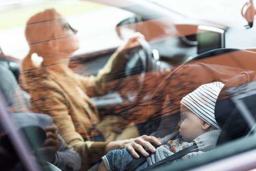 Mother concentrating on driving family car running errands while her baby sleeps in infant car seat by her site