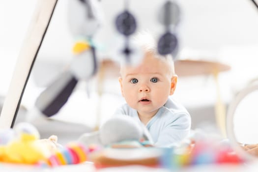 Cute baby boy playing with hanging toys arch on mat at home Baby activity and play center for early infant development. Baby playing at home.