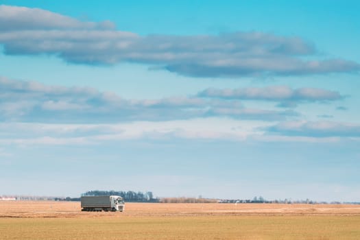 Truck Or Tractor Unit, Prime Mover, Traction Unit In Motion On Road, Freeway. Asphalt Motorway Highway Against Background Of Spring Meadow Field Landscape. Business Transportation And Trucking Industry