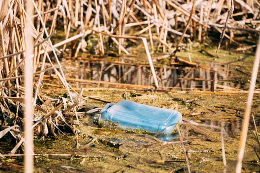 Old Plastic Canister Floats In Water Of Swamp Or Pond. Used Empty Packing Materials Left In Water. Eco Concept Garbage Disaster From Ecological Pollution Of Environment. Waste Pollution Problem.