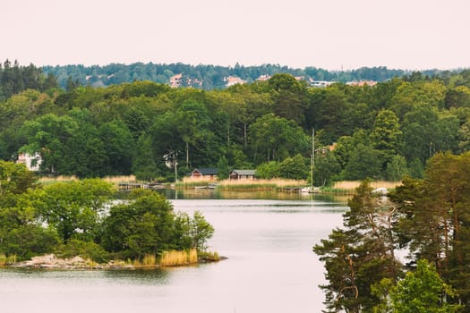 Sweden. Beautiful Swedish Wooden Log Cabins Houses On Coast In Summer Day. Lake Or River Landscape.