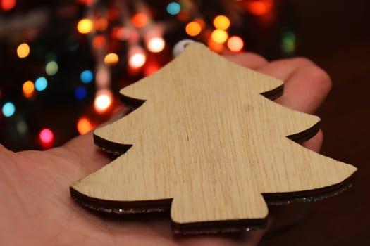 Christmas tree made of handmade wood in a female hand against the background of a Christmas garland. Concept of christmas, new year, ecology.