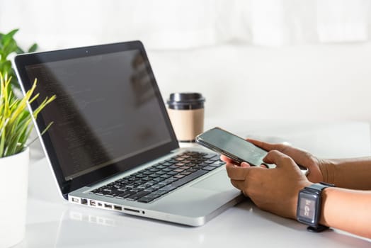 Programmer woman looking mobile phone program code at workplace, software developer hands typing data coding programming javascript with laptop computer, IT startup concept, Web application design