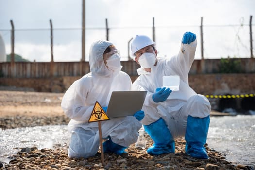 Ecologist sampling taken dead fish to inspaction and save data to laptop computer, Biologist wear protective suit and mask collects sample of waste water from industry, problem environment