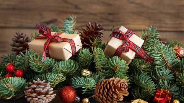 Wrapped gift boxes on reen fir branches near Christmas decorations and pine cones close up on wooden background, copy space. Christmas or New Year Holiday atmosphere