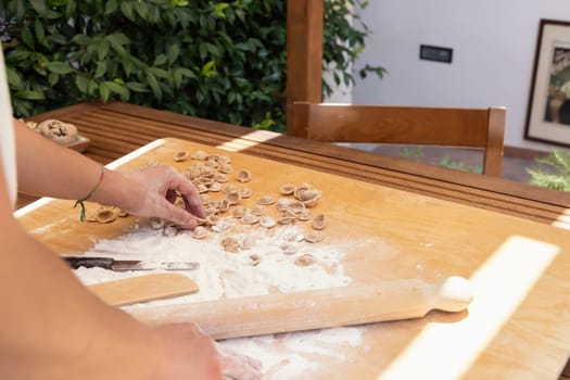 Woman makes south italian pasta orecchiette outdoor in the house yard close up. Traditional fresh homemade pasta of apulia region. Mediterranean diet ingredient. Local cousine