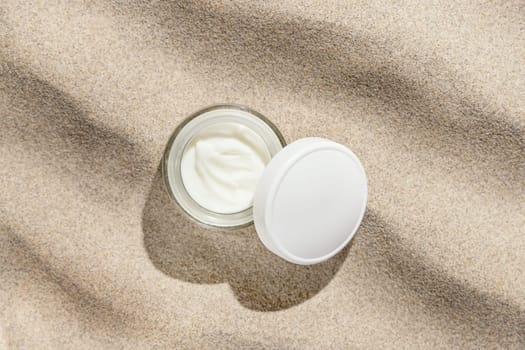Opened cream jar with white lid on beige sand top view, hard light. Package mockup. Natural skincare product. Facial cosmetics for beauty routine. Zen style, minimal aesthetic