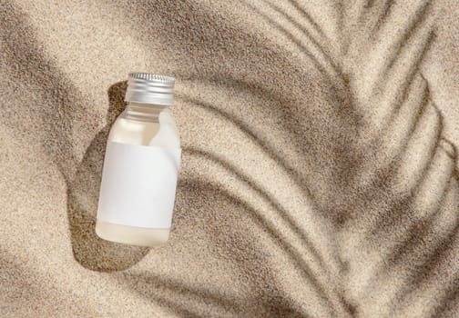 Cosmetic Cream bottle with blank label on beige sand top view. Packaging mockup. Natural skincare product for beauty routine. Summer sunny day with palm leaf hard shadow, tropical vacation mood